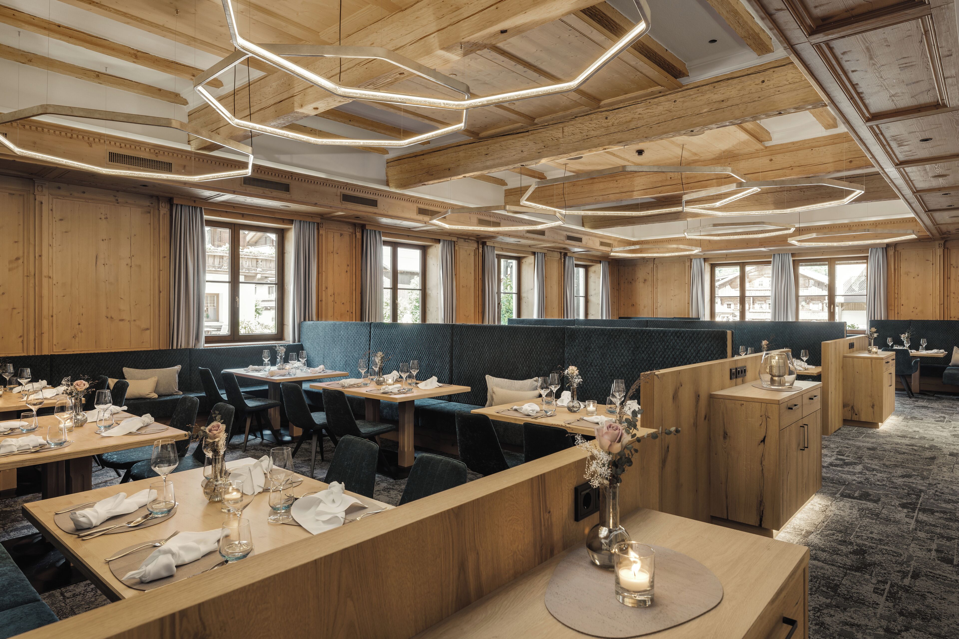 Un restaurante con mesas y cabinas de madera, dispuesto en un espacio amplio con ventanas grandes que dejan entrar luz natural.