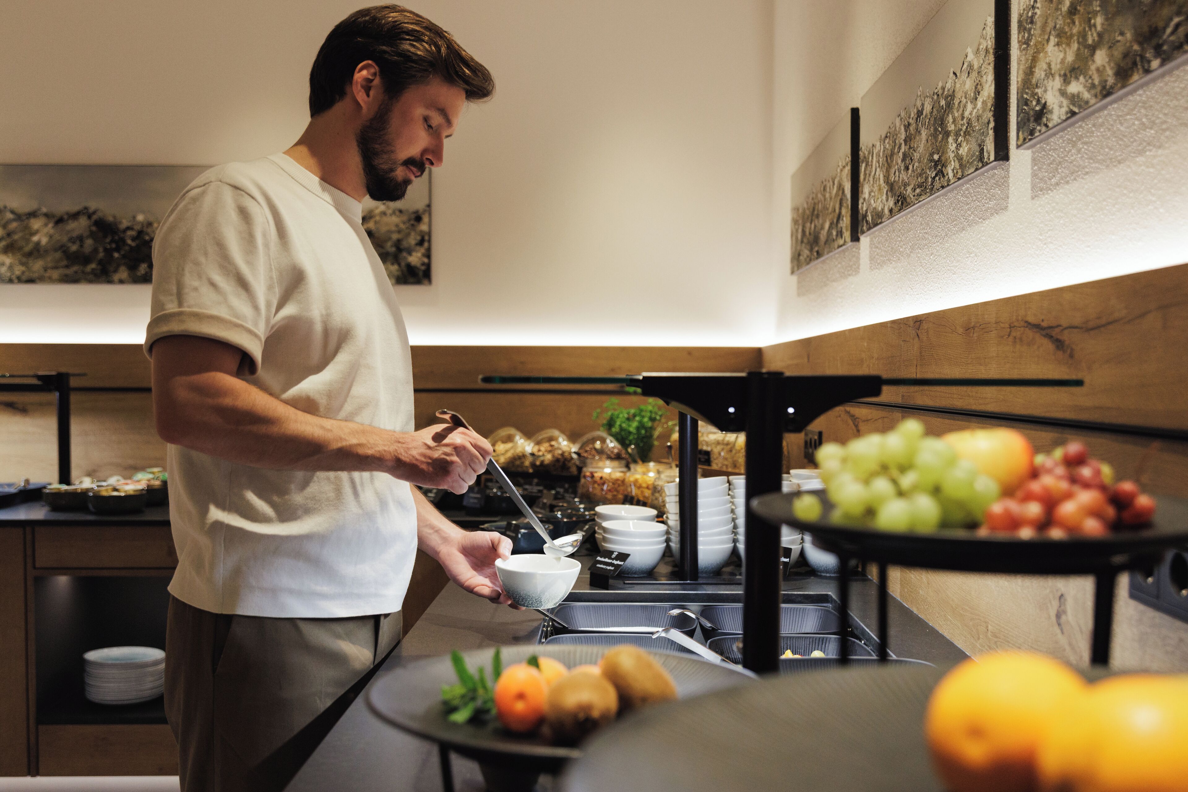 Montaje de buffet con diversas frutas y verduras, una persona sirviendo comida, y una decoración interior moderna.