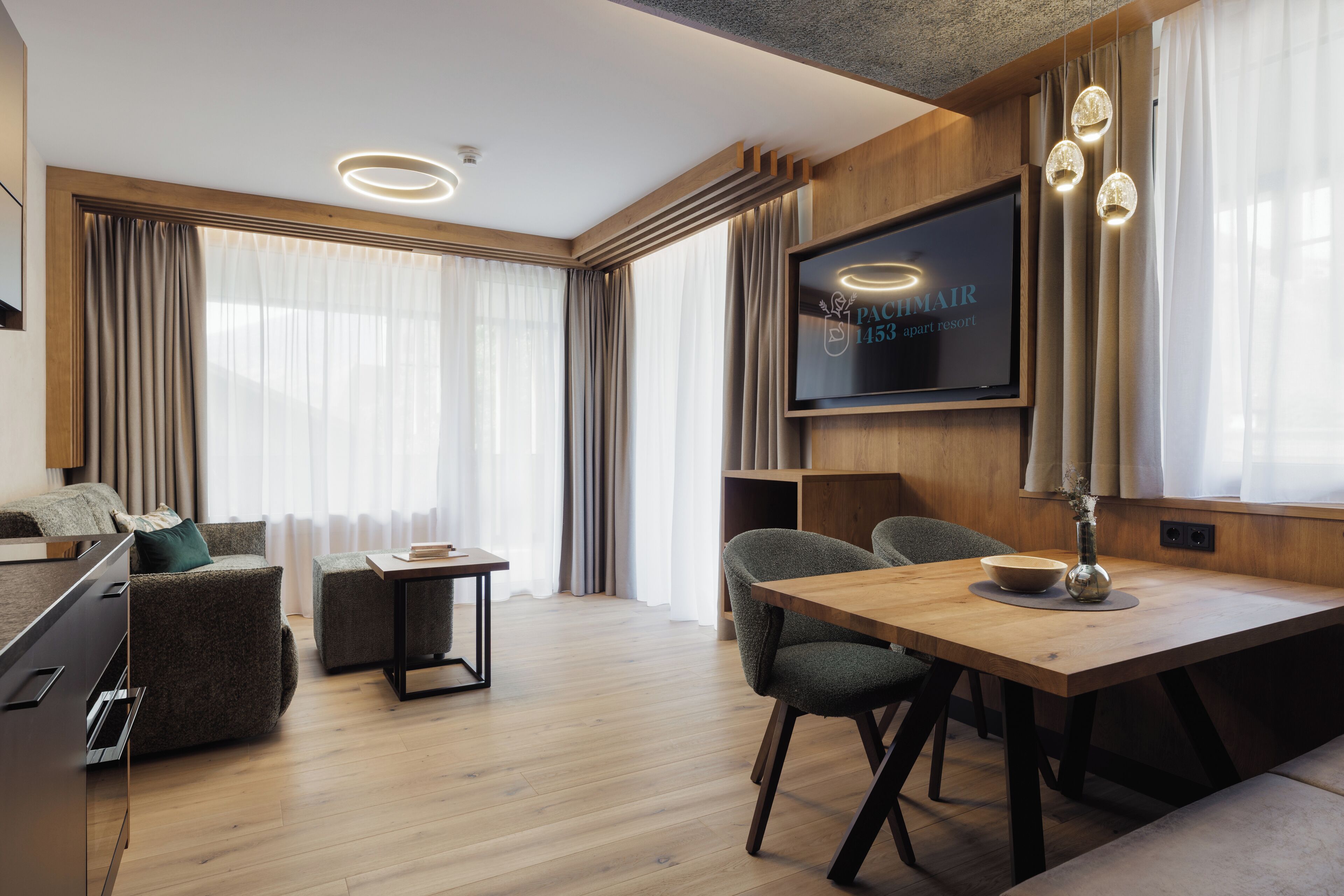 Una habitación de hotel moderna con piso de madera, un televisor de pantalla plana en la pared, una mesa de comedor con sillas y un sofá.