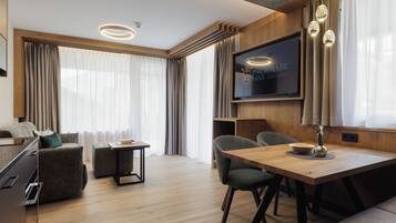 Una habitación de hotel moderna con piso de madera, un televisor de pantalla plana en la pared, una mesa de comedor con sillas y un sofá.
