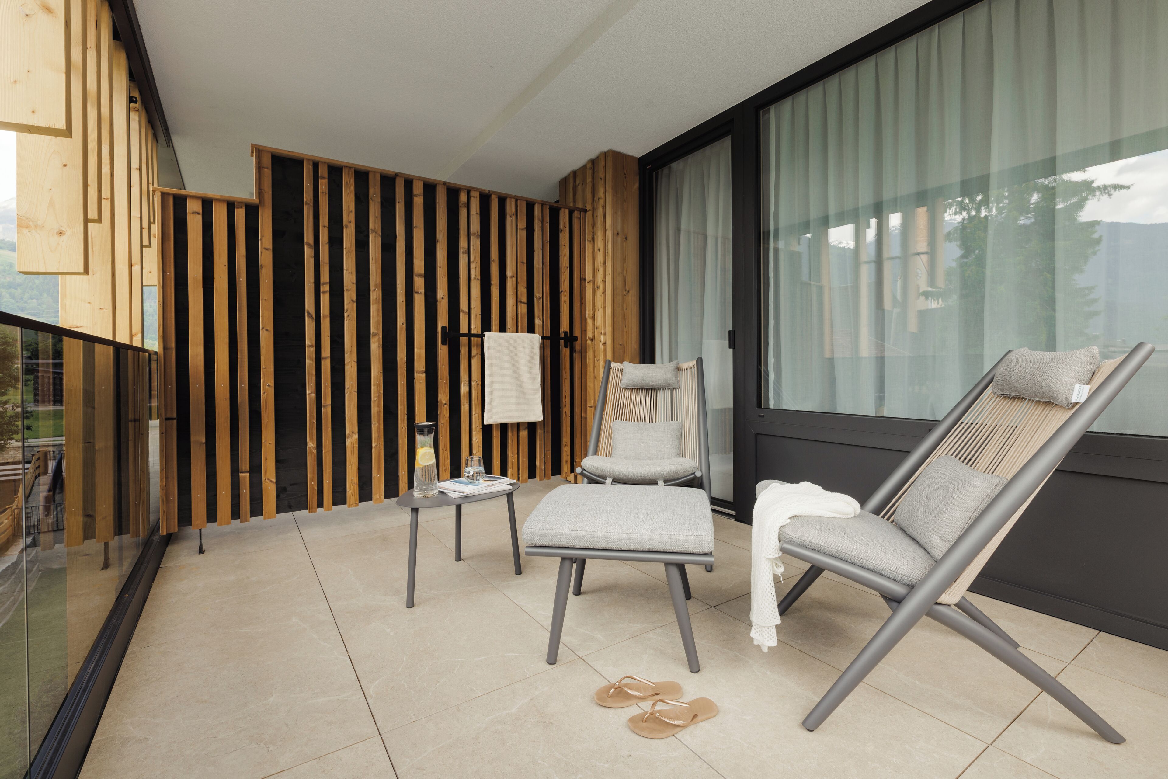 Un balcón moderno con pared de listones de madera, puerta de cristal y dos sillones de relax.
