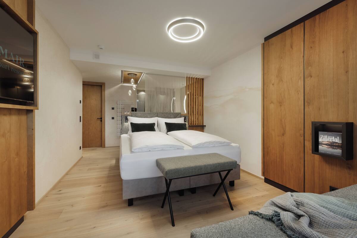 A modern bedroom with a bed, bedside tables, a bench, and a TV screen.
