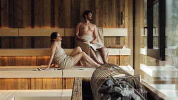A wooden spa room with two people sitting on benches, a wooden wall, and a window.