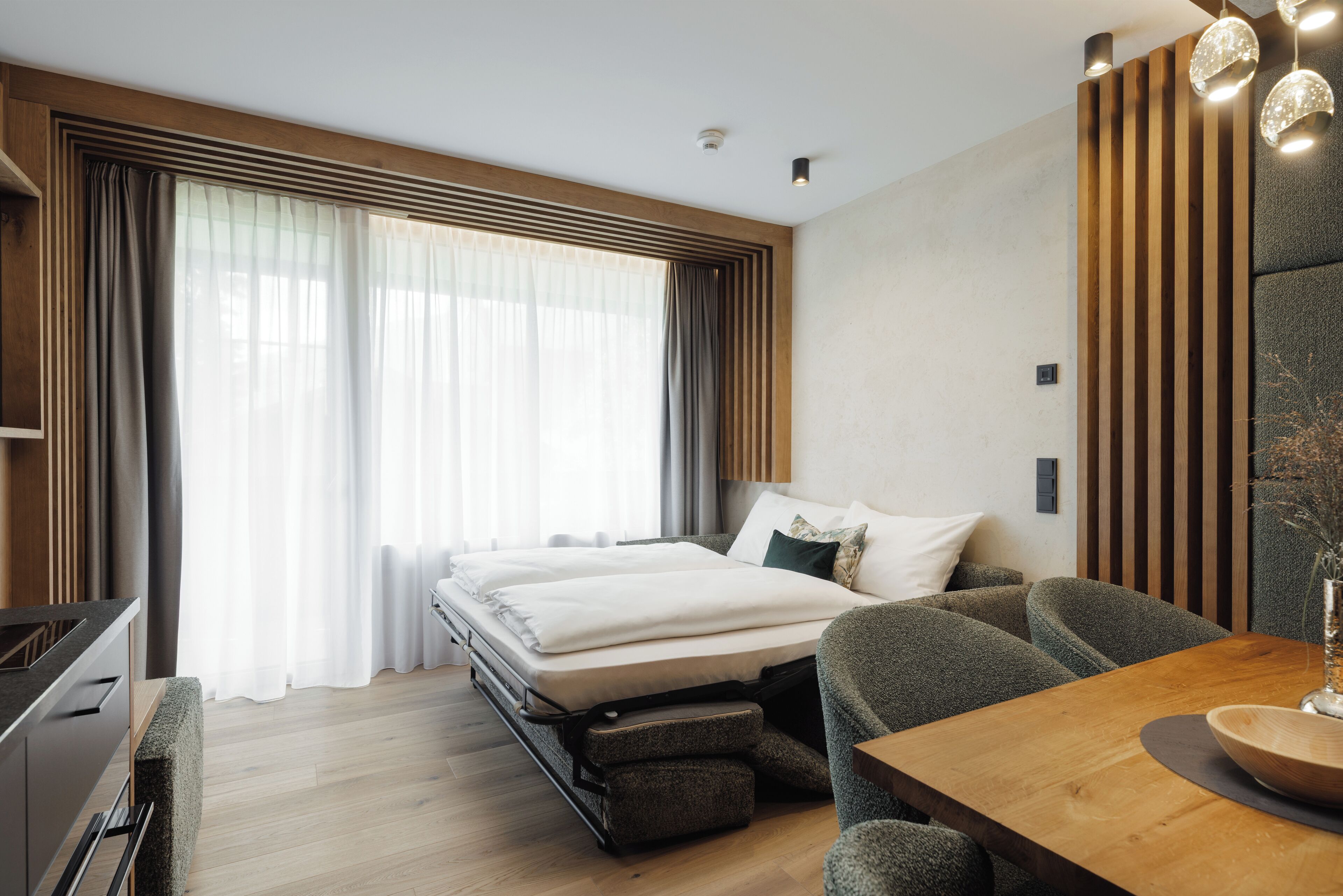 A modern hotel room with a bed, seating area, and a dining table.