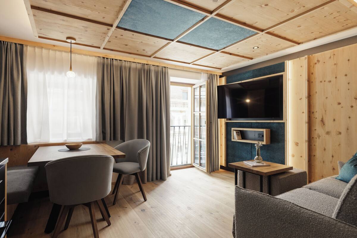 A modern living room with a wooden ceiling, a flat-screen TV mounted on a wall, a sofa, and a dining area with a table and chairs.