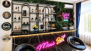 Un espace bar avec des étagères remplies de bouteilles d’alcool, un panneau néon indiquant « Mini Bar » et une enseigne « Central Hotel ».