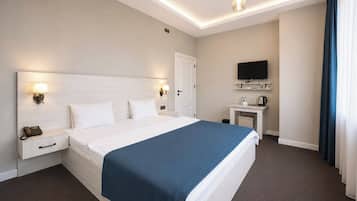 Una habitación de hotel con una cama grande, mesitas de noche, un escritorio con televisor de pantalla plana y una lámpara en el techo.
