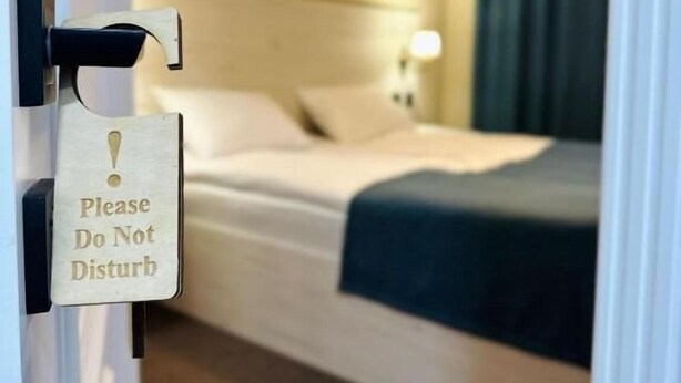 Une chambre d’hôtel avec un lit, une table de chevet avec une lampe et une porte sur laquelle est accrochée une pancarte indiquant : « Veuillez ne pas déranger ».