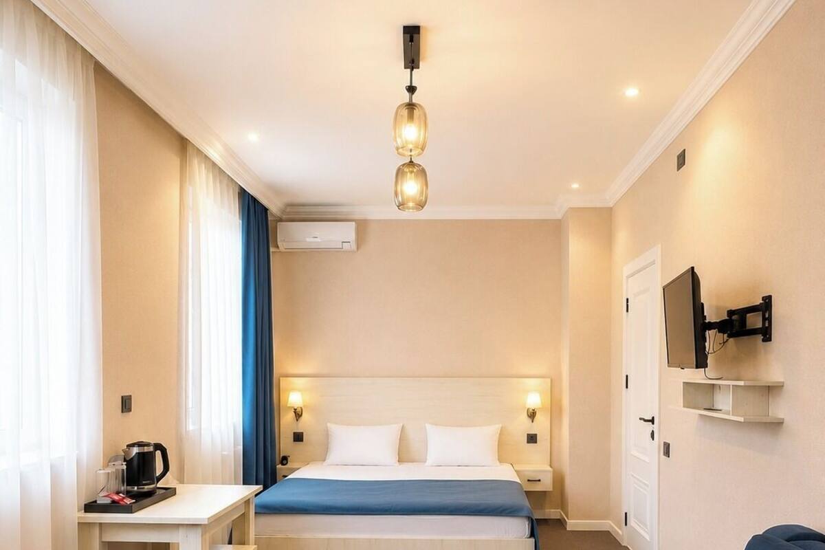 A hotel room with a bed, bedside tables, a desk, a chair, a TV, and a sofa.