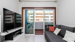 A modern living room with a flat-screen TV, grey sofa, and a sliding glass door leading to an outdoor balcony. - Platan Apartment, Portimão, Algarve (Portimão)