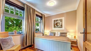 Un dormitorio con una cama grande, una silla, un ventanal con cortinas y una obra de arte colgada en la pared.
