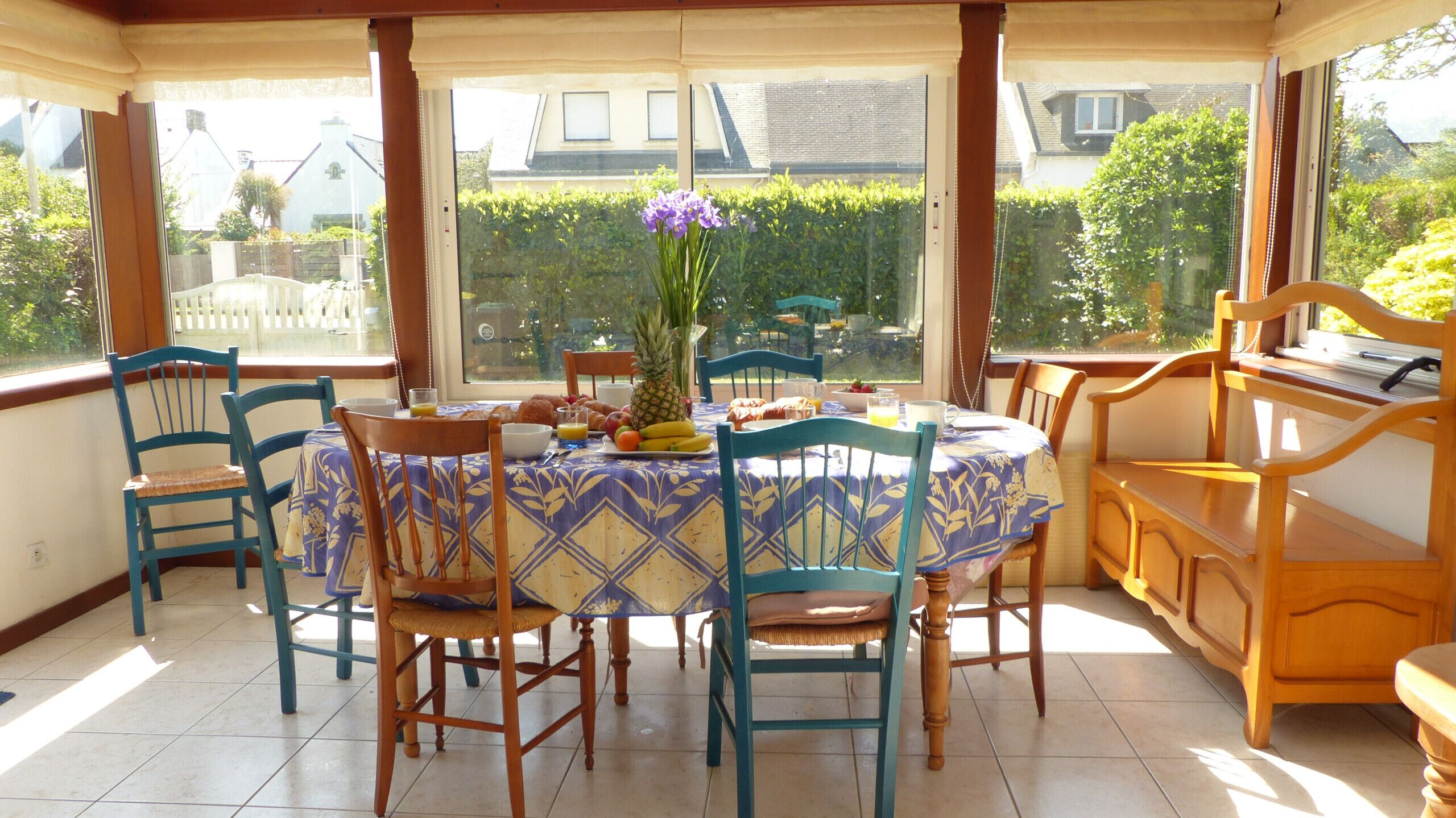 A sunlit dining area with a round table, blue chairs, and a wooden bench.