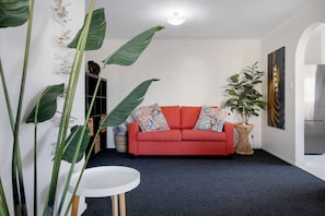 A living room with a red sofa, a round white table, and a large plant. - Sunny Surfers Stay - Beach & Tram at your doorstep (Surfers Paradise)