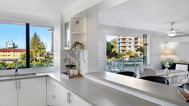 A modern kitchen with a large window, white cabinetry, and a dining area with a table and chairs.
