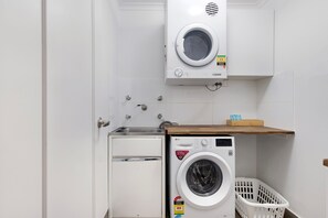A compact laundry room with a washing machine, a dryer, and a small storage cabinet. - Sunny Surfers Stay - Beach & Tram at your doorstep (Surfers Paradise)