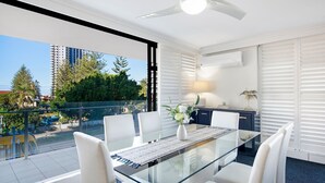 A modern dining area with a glass table, white chairs, and a ceiling fan.
