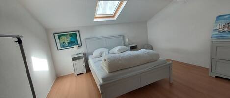 Une chambre à coucher avec un puits de lumière, un lit, une table de chevet, une commode, une lampe et un tableau.