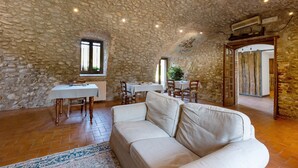 A stone-walled room with a white sofa, dining table, chairs, and a ceiling with a stone pattern.