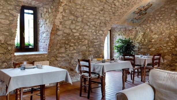A stone-walled dining area with tables and chairs, a window with a view, and a mural on the ceiling.
