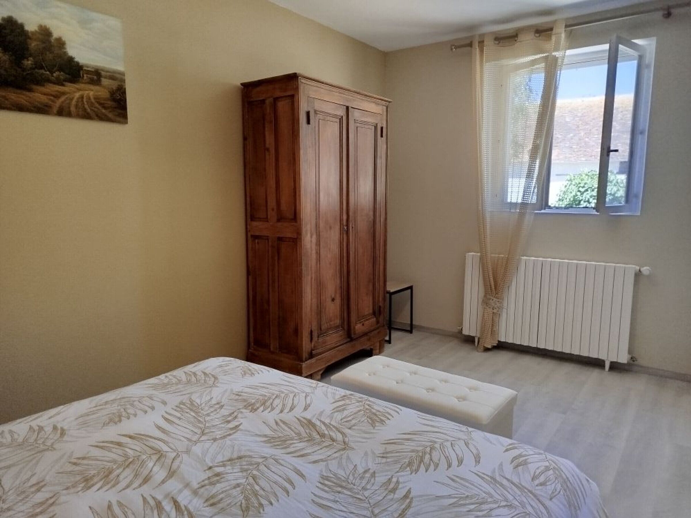 A bedroom with a bed, a wooden wardrobe, a radiator, and a window with curtains.