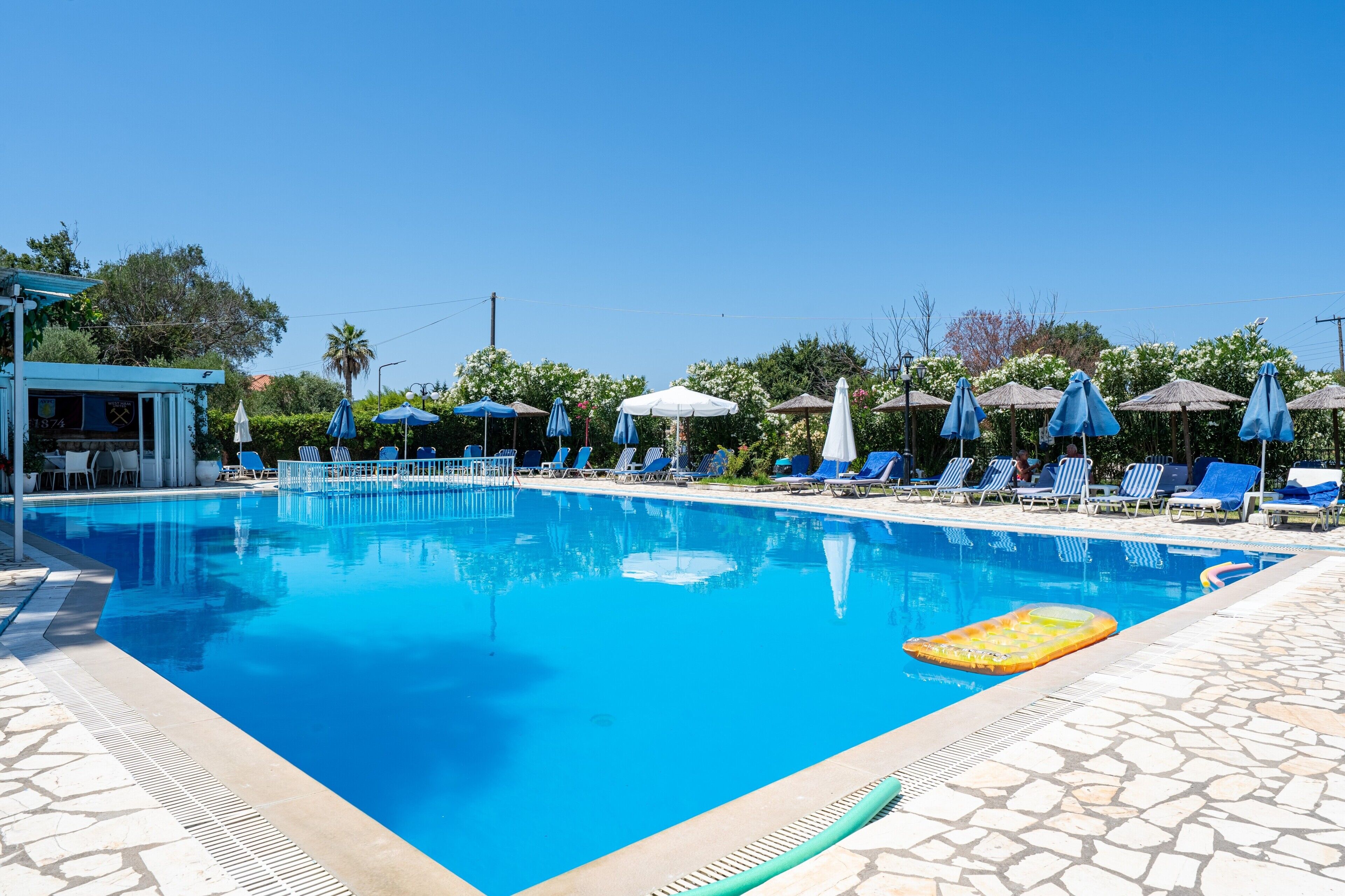 Uma piscina com espreguiçadeiras e guarda-sóis, cercada por azulejos de pedra e vegetação.