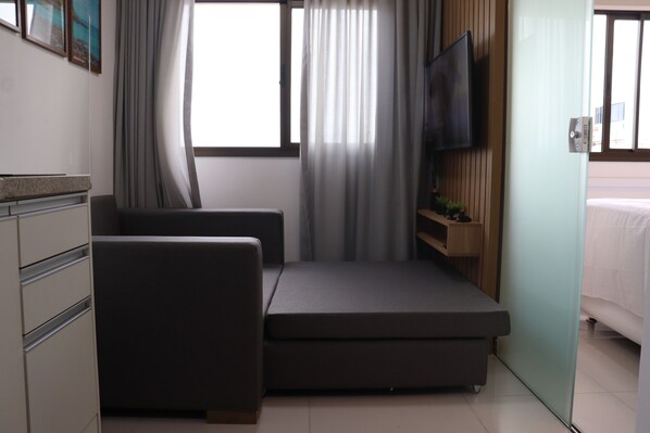 A modern hotel room with a bed, a sofa, a TV, and a window with curtains.