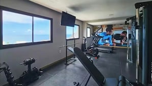 Un gimnasio con equipo de ejercicio, una televisión y amplias ventanas.