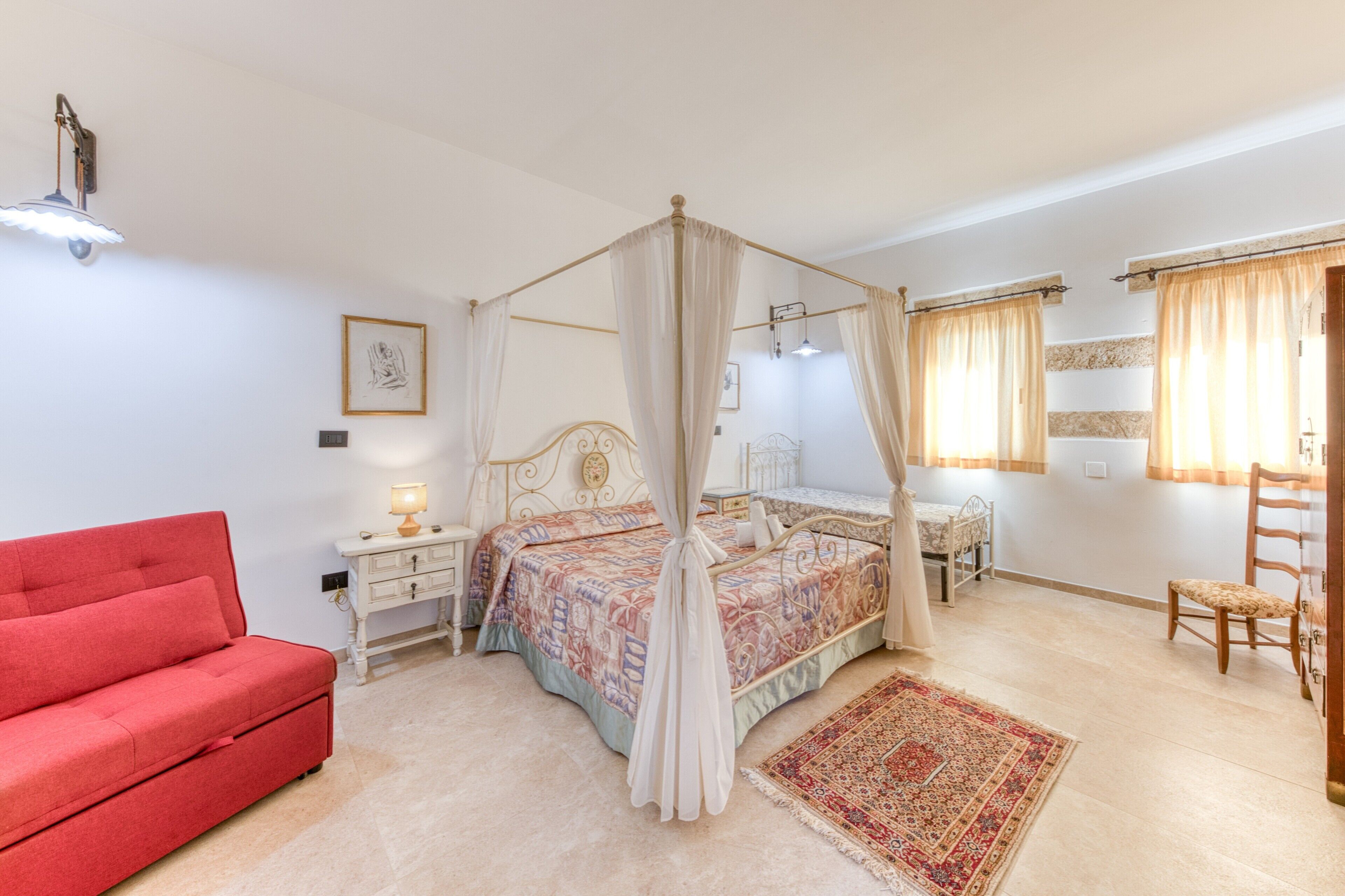 Une chambre à coucher avec un lit à baldaquin, un canapé rouge, une table de chevet avec une lampe, une chaise en bois et un grand tapis.