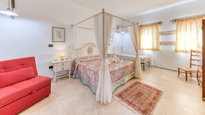 A bedroom with a four-poster bed, a red sofa, a nightstand with a lamp, a wooden chair, and a large rug.