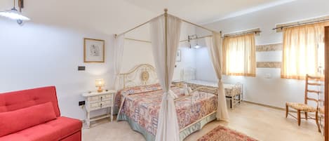 Un dormitorio con cama con dosel, un sofá rojo, una mesita de noche con lámpara, una silla de madera y una alfombra grande.