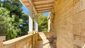 A covered outdoor area with a stone wall, a table with chairs, and a view of trees.