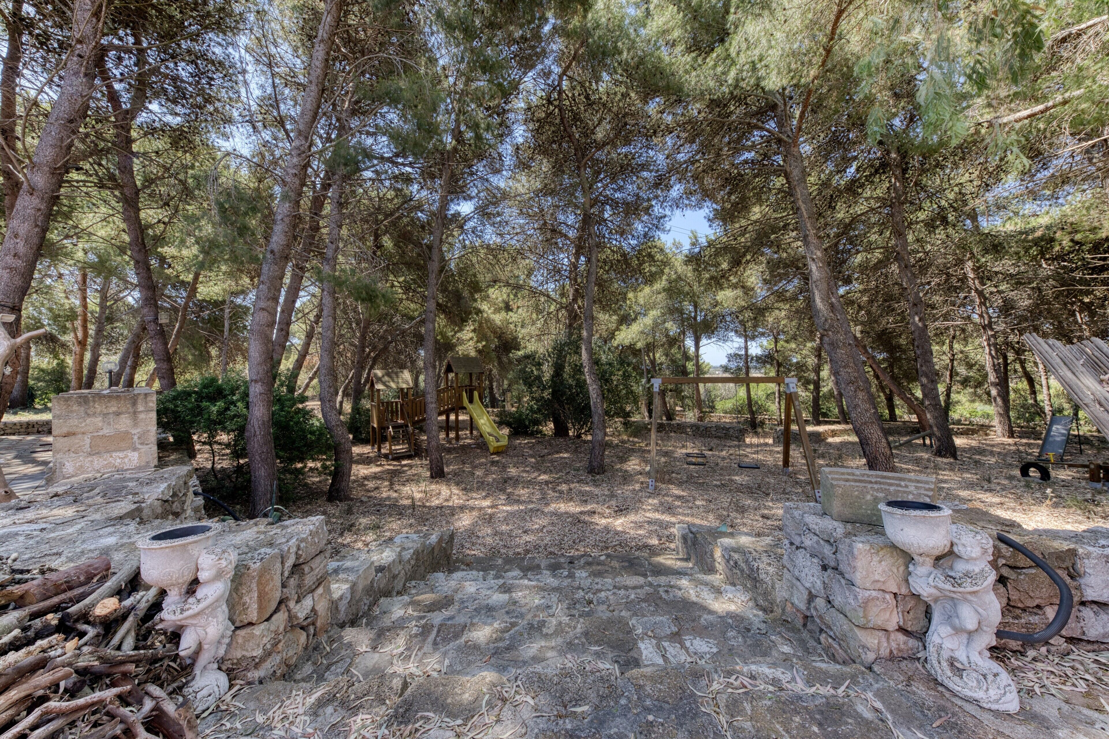 Un sentier de pierres qui traverse une zone boisée, avec des arbres et une structure en bois en arrière-plan.