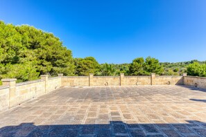 A stone-paved terrace with a stone wall and a view of a forested hillside.