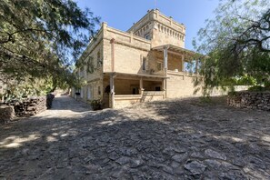 Ein Gebäude aus Stein mit einem Balkon, einem Kiesweg und Bäumen.