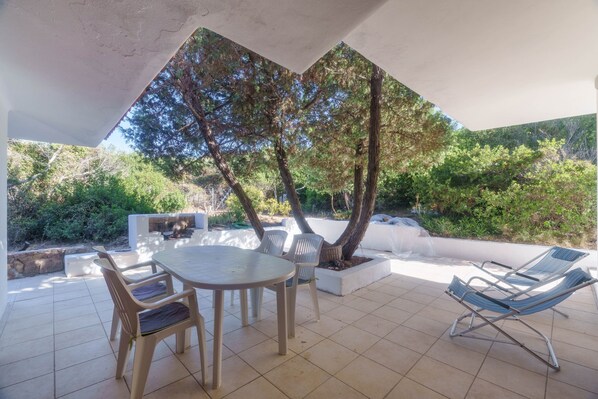 An outdoor patio with a table and chairs, a hammock, and a tree in the background.