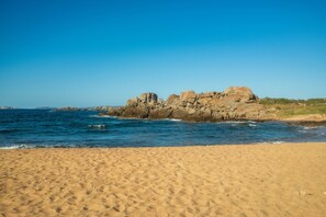 A beach with a rocky outcrop in the distance and clear blue skies.
