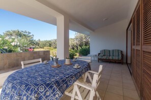 A covered patio with a table set for dining, a sofa, and a view of the surrounding greenery.