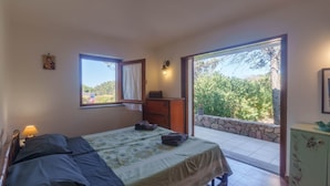 A bedroom with a bed, a nightstand, a dresser, a window, and a balcony with a stone wall. - Holiday Home 'Mirella- Portobello' with Private Terrace, Private Garden and Wi-Fi (Portobello)