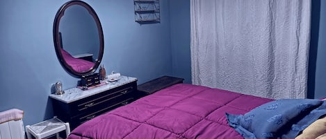 A bedroom with a bed, a dresser, a mirror, a television, and a window with curtains.