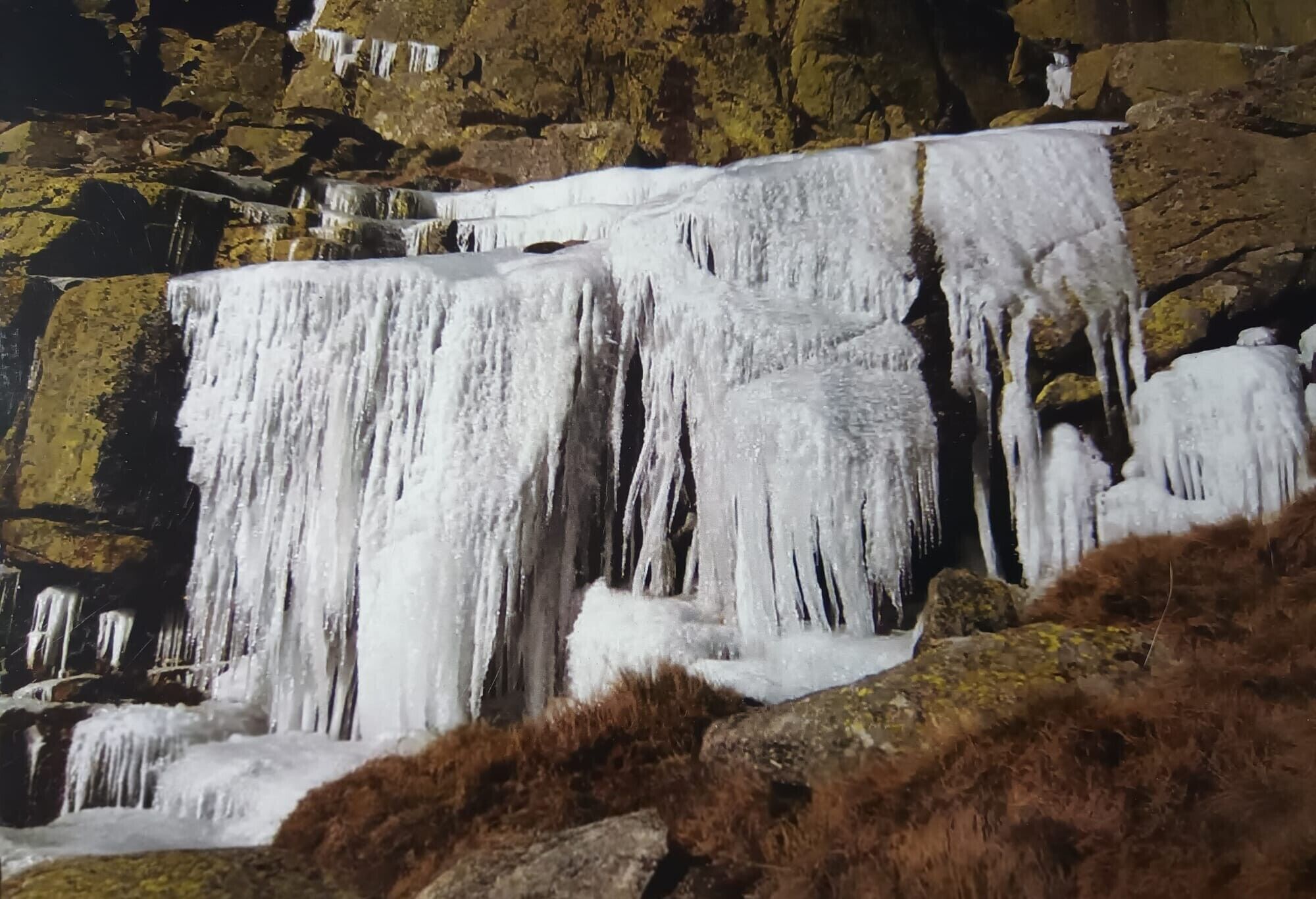 Una cascada fluye sobre terreno rocoso con estalactitas colgando de los bordes.