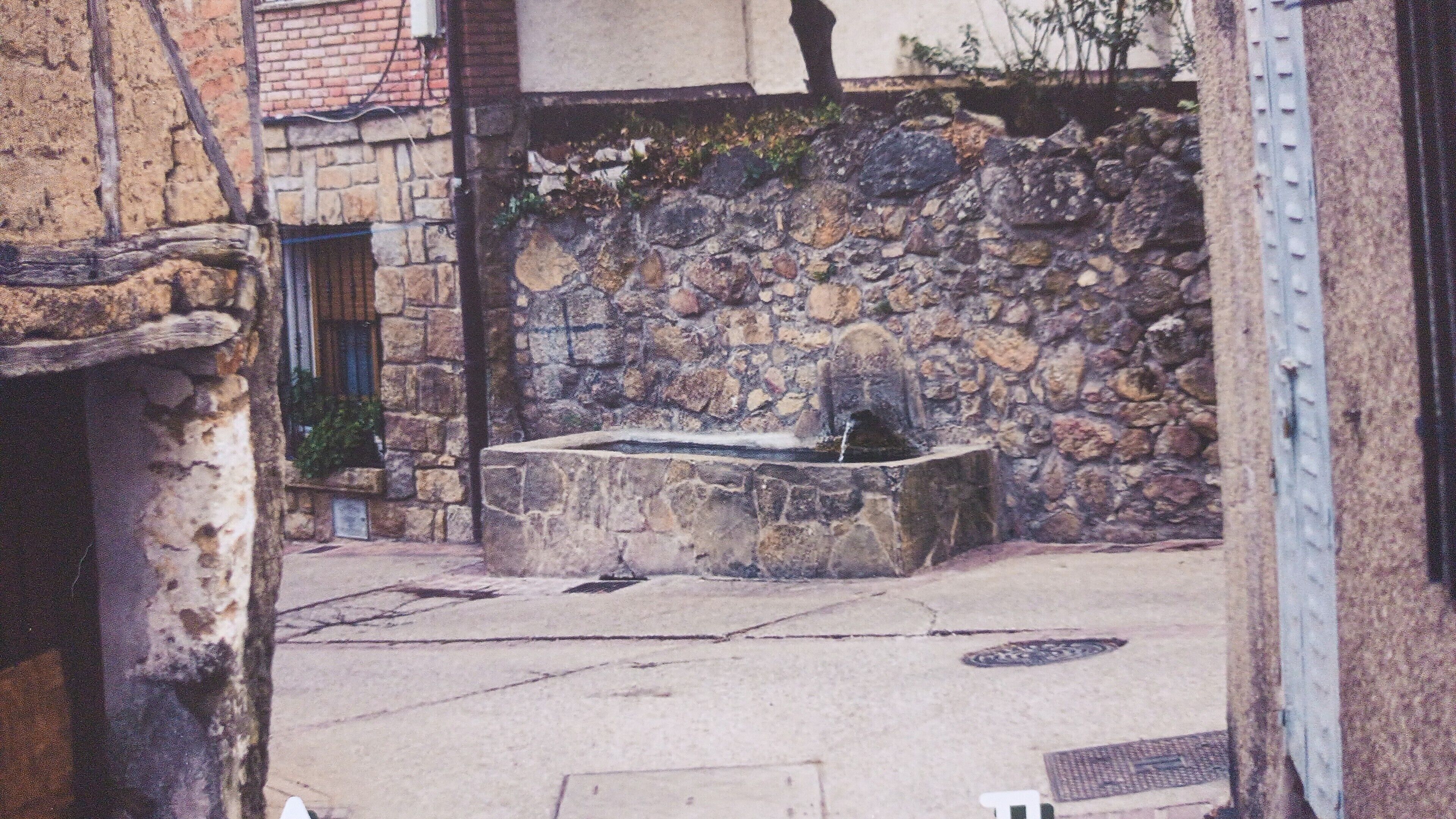 Ein Steinkunstbrunnen in einem Innenhof mit einer Steinmauer und einem Metallgitter.