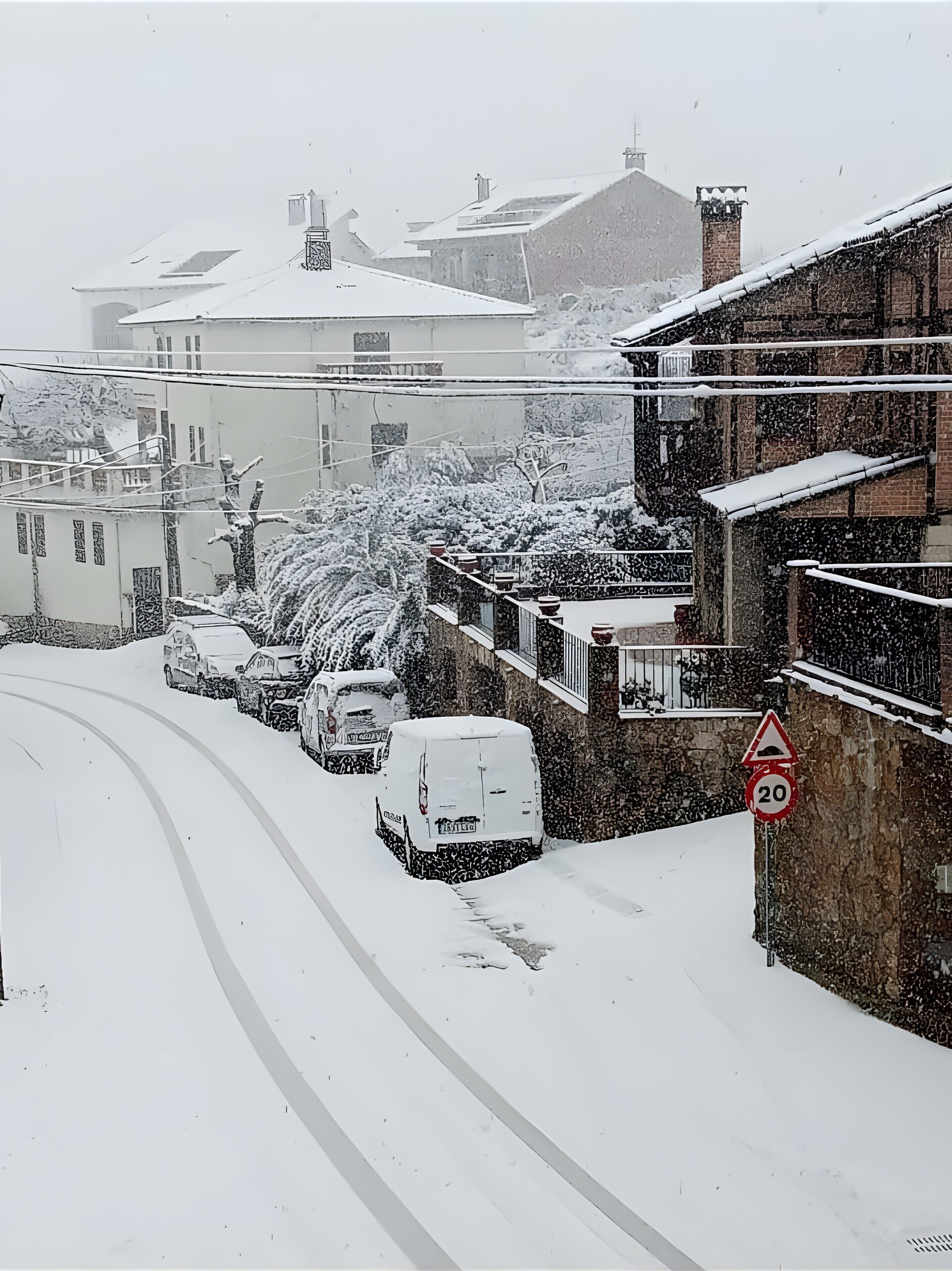 Una calle nevada con coches aparcados y edificios.