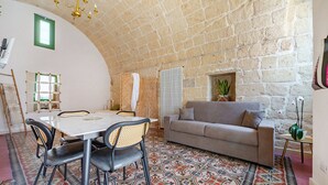 A room with a stone wall, a round table with chairs, a sofa, and a patterned floor.