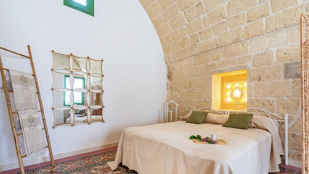 A bedroom with a bed, a mirror, a window, and a patterned floor.