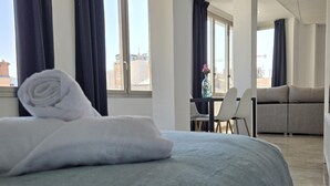 A hotel room with a bed, a sofa, a dining table, and a view of the city. - Modern Suites in Malaga Center (Málaga)