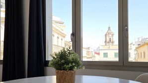 Et værelse med et rundt bord, en potteplante og et vindue med udsigt til en bygning med et klokketårn.