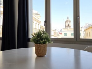 A room with a round table, a potted plant, and a window with a view of a building with a bell tower. - Design Suites in Malaga Center, max 4 guests (Málaga)