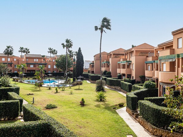 A hotel courtyard with a swimming pool, palm trees, and neatly trimmed hedges.