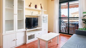 A compact living space with a TV, white cabinets, a small table, and a sliding glass door to an outdoor area. - Charming apartment in Chiclana with pool and parking (Chiclana de la Frontera)