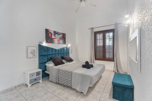 A bedroom with a bed, a nightstand, a ceiling fan, a window with curtains, and a painting on the wall.